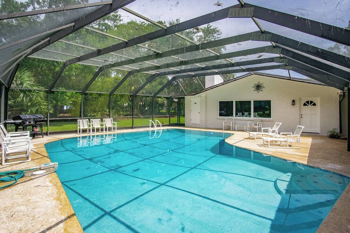 Une piscine couverte avec un espace patio, des chaises longues et un barbecue.