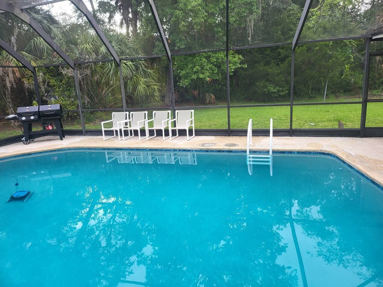 A swimming pool with a glass enclosure, surrounded by chairs and a barbecue grill.