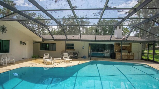 A swimming pool with a covered patio area, outdoor seating, and a view of the surrounding landscape. - Gem at Crystal River (Crystal River)