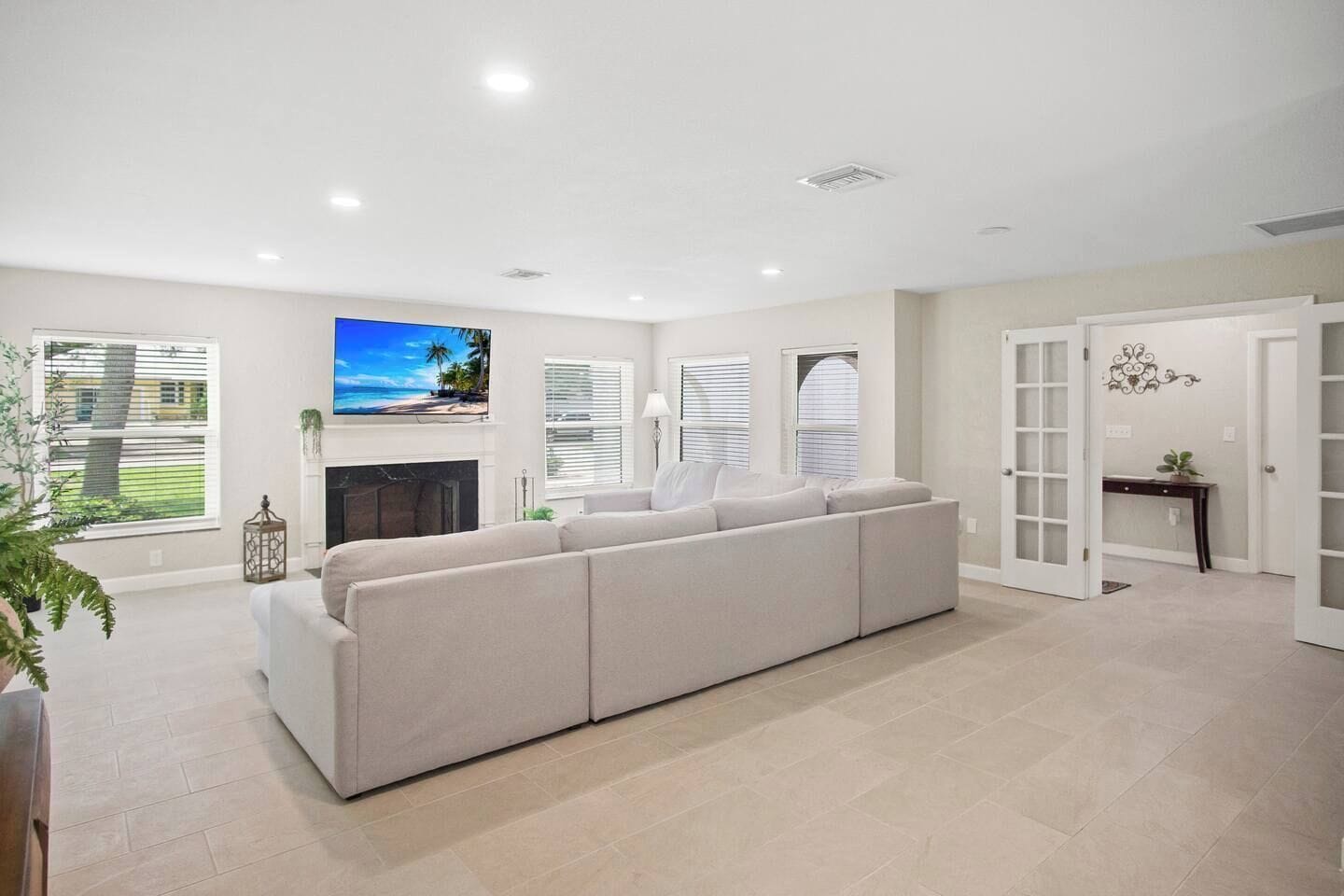 A modern living room with a large beige sectional sofa, a fireplace, and a view of a beach through the windows.