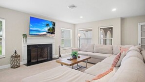 A living room with a fireplace, a large flat-screen TV mounted above it, a sofa, and a coffee table. - Gem at Crystal River (Crystal River)
