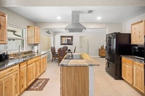 A modern kitchen with wooden cabinets, granite countertops, a central island, and a black refrigerator. - Gem at Crystal River (Crystal River)