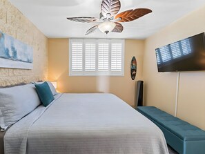 Un dormitorio con cama, ventilador de techo, televisor y ventana con persianas.