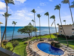 A pool area with a view of the ocean, surrounded by palm trees and a building. - Maalaea, Kanai A Nalu, Spacious 4 BR, Beachfront, Sleeps 12 (Wailuku)