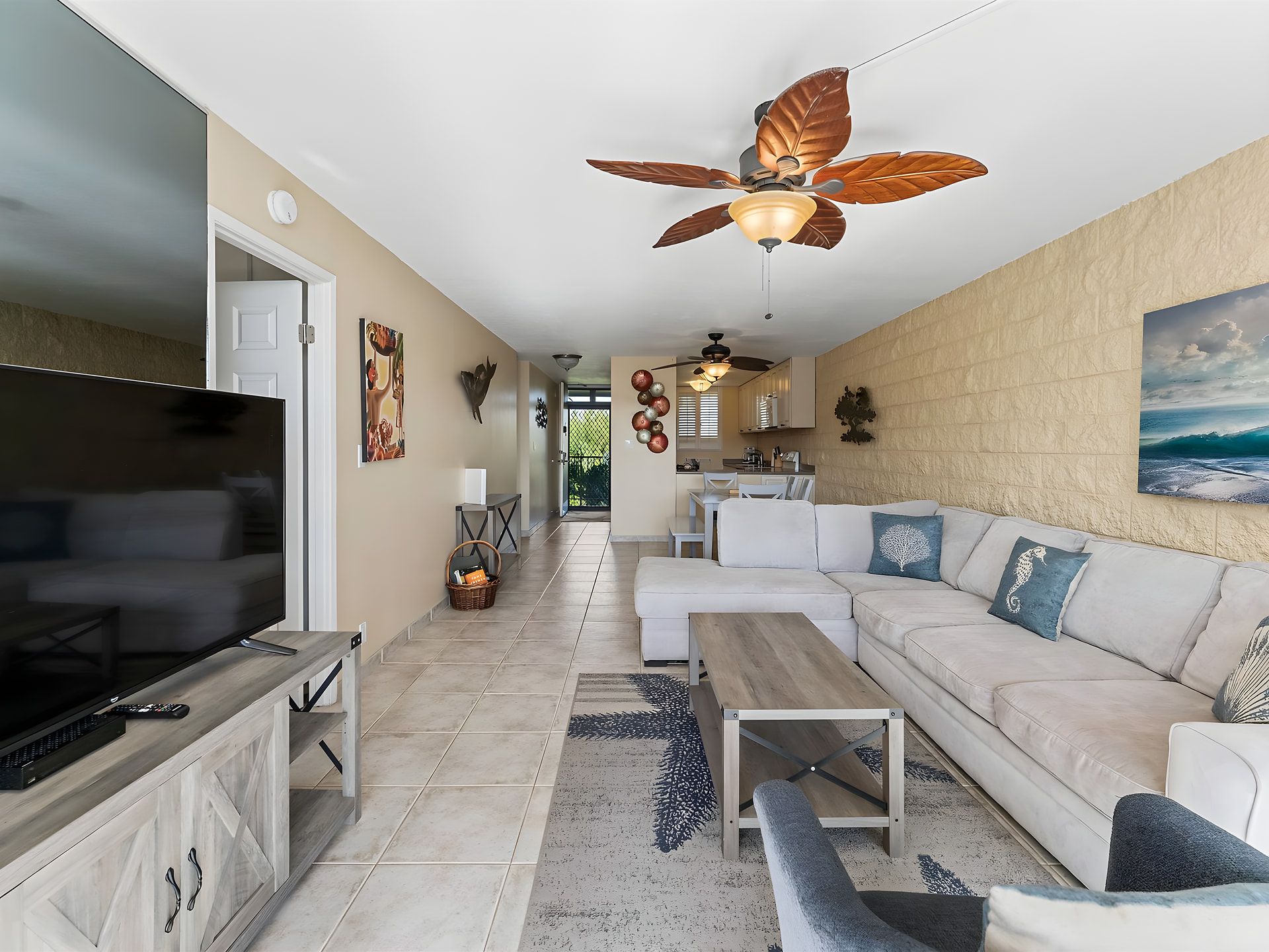 A modern living room with a flat-screen TV, a sofa set, a coffee table, and a ceiling fan.