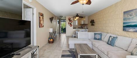 A modern living room with a flat-screen TV, a sofa set, a coffee table, and a ceiling fan.