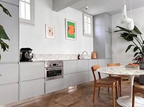 A modern kitchen with built-in appliances, a dining area with a marble table, and a large window providing natural light. - Chic and quiet Parisian apartment with an elevator, near the Grands Boulevards (Paris)