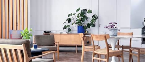 Een moderne woonkamer met een bank, stoelen, een eettafel en een grote plant.