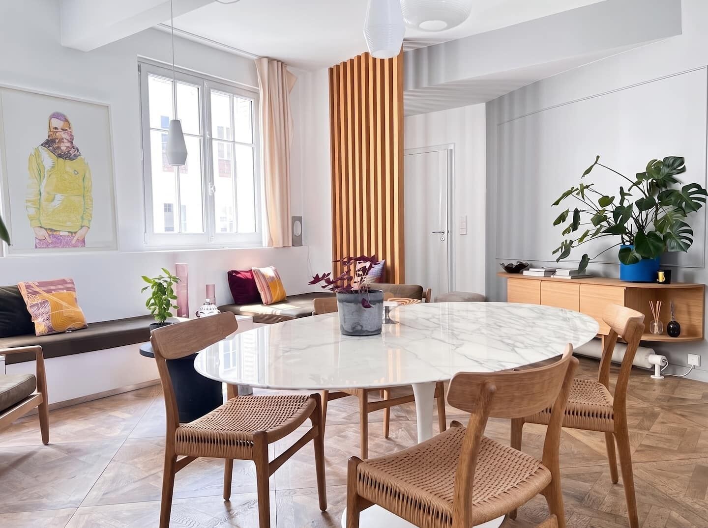 A modern dining area with a round marble table, wooden chairs, and a vertical wooden panel.