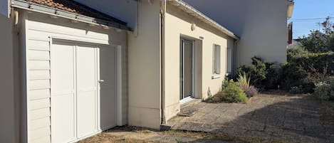Un edificio de dos pisos con garaje, un porche cubierto y un pequeño jardín.