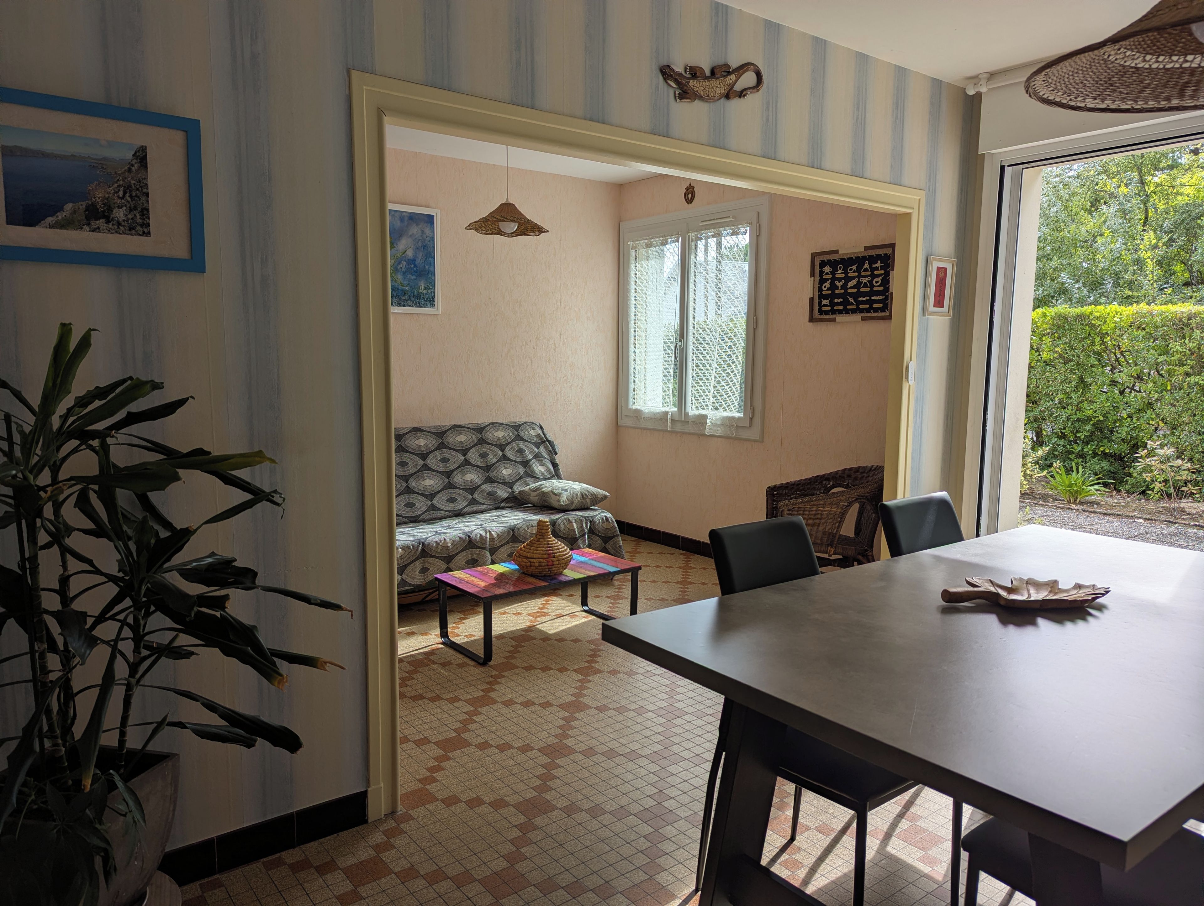 Une pièce comprenant une table à manger, des chaises, un canapé, une plante en pot et une fenêtre donnant sur un paysage verdoyant.
