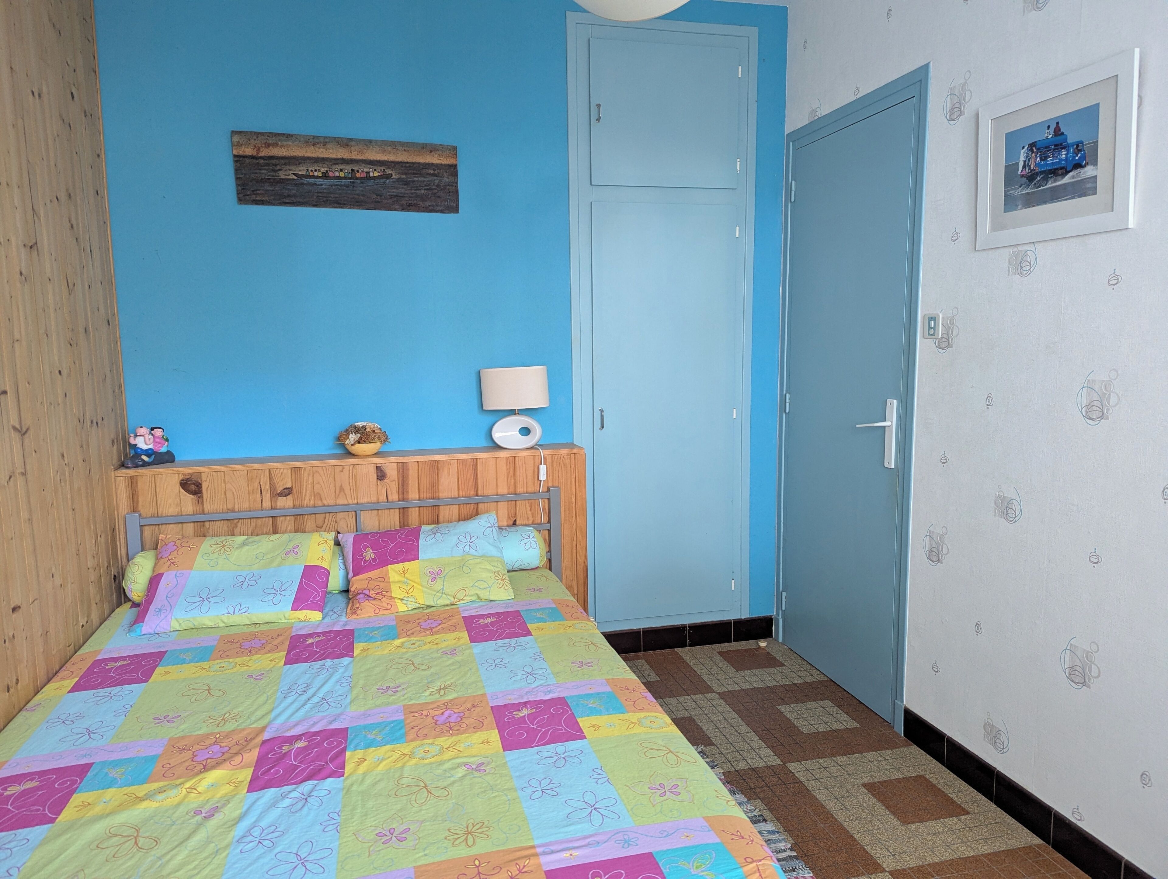 A bedroom with a bed, a wooden headboard, a blue door, and a wall-mounted lamp.