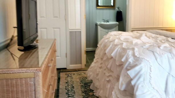 Un dormitorio con cama, cómoda, televisor, puerta, espejo y un baño visible a través de una puerta abierta.