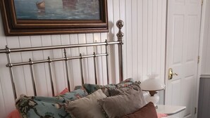 Una cama con ropa de cama estampada con motivos florales, un cabecero de metal y un cuadro en la pared superior.