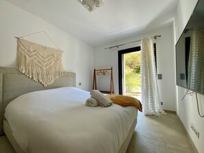 A bedroom with a large bed, a macrame wall hanging, a wooden hanger rack, and a large window with curtains. - Welcome to Le Jardin des Cambrettes, a 2-hectare private estate at the gate (Lattes)