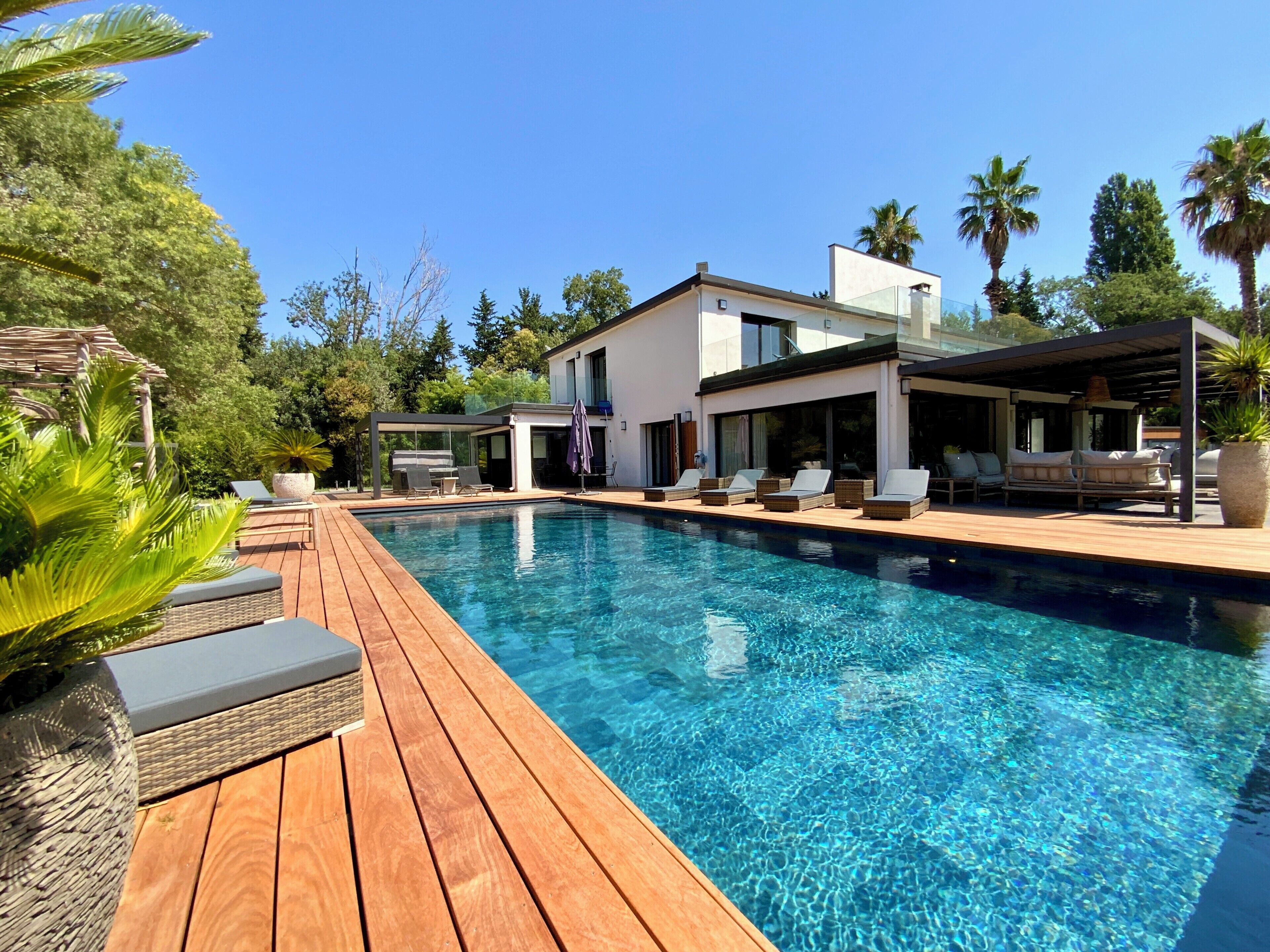 Ein moderner Poolbereich mit Holzterrasse, Liegestühlen und einer überdachten Sitzgruppe.