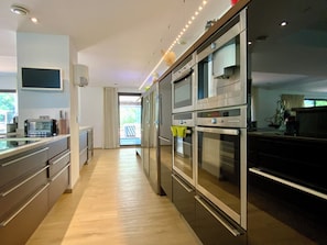 A modern kitchen with stainless steel appliances, a flat-screen TV, and a sliding glass door leading to a balcony. - Welcome to Le Jardin des Cambrettes, a 2-hectare private estate at the gate (Lattes)