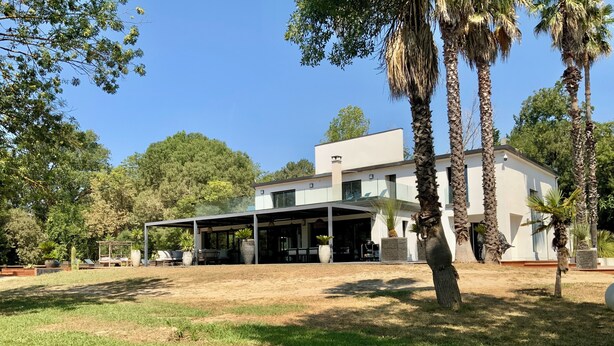 Ein modernes Haus mit überdachter Terrasse, umgeben von Bäumen und einem Rasen.