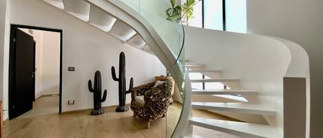 Un intérieur moderne avec un plancher en bois, un escalier en verre et une décoration à base de cactus.