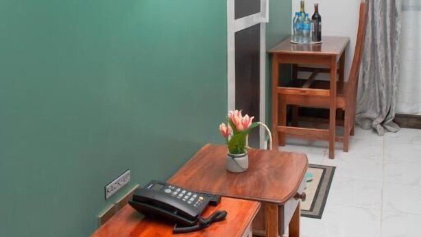 Ein Zimmer mit an der Wand montiertem Fernseher, einem Holztisch mit Telefon, einer kleinen Vase mit Blumen und einer Tür zu einem anderen Raum.