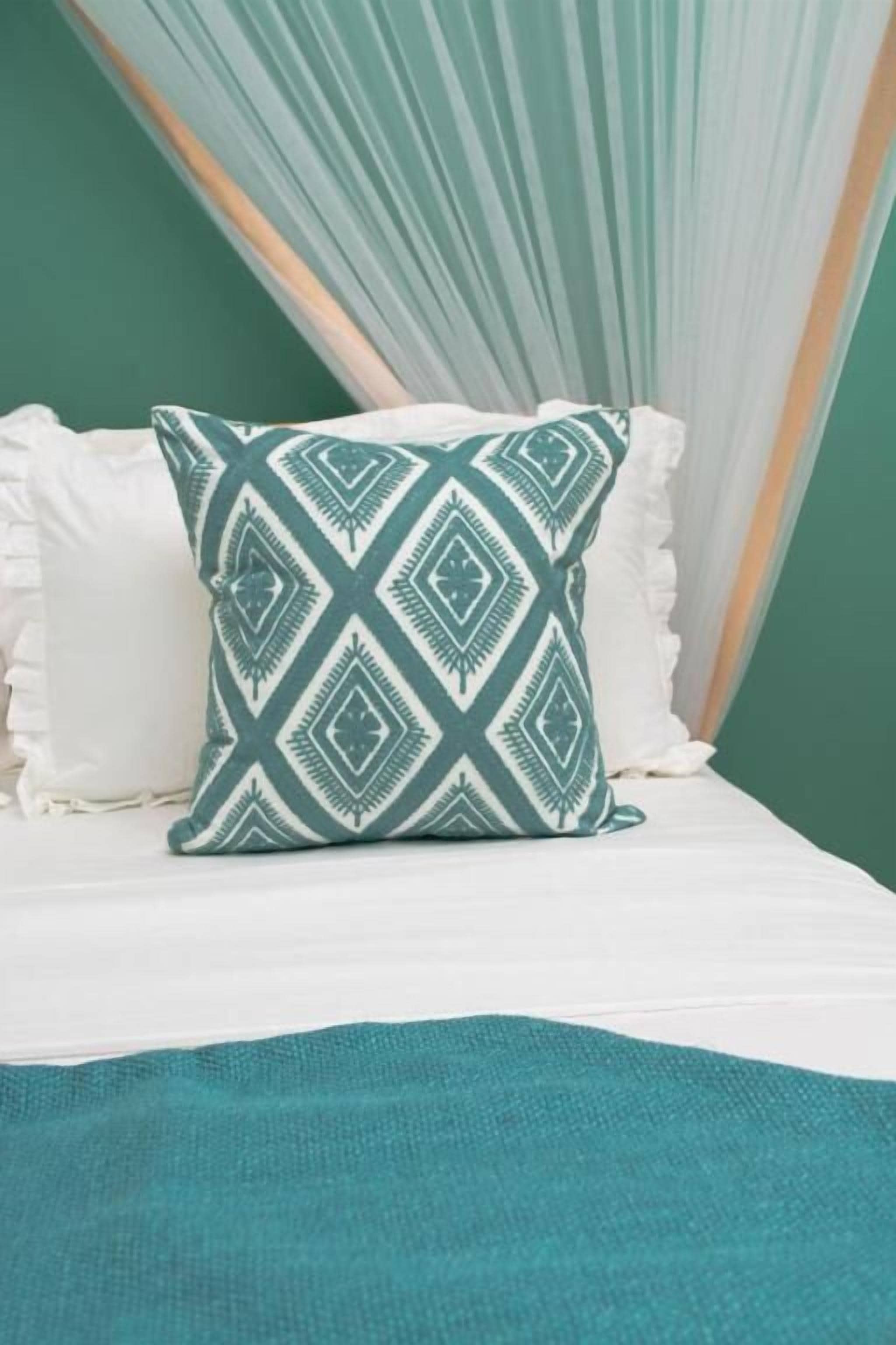 Uma cama com um travesseiro estampado, um travesseiro branco e um cobertor azul-turquesa.