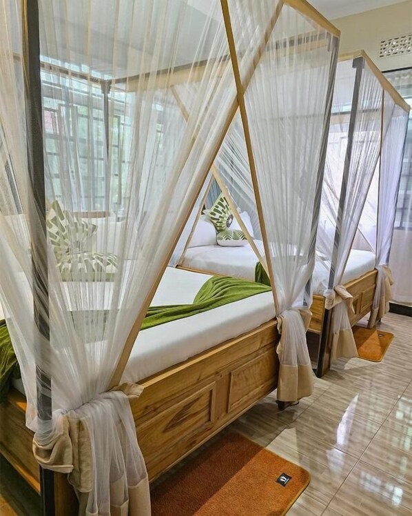 A room with four beds, each with a canopy and a wooden headboard.