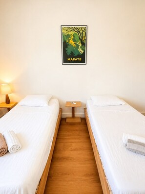Ein Zimmer mit zwei Einzelbetten, einem kleinen Nachttisch mit Lampe und einem Poster an der Wand.