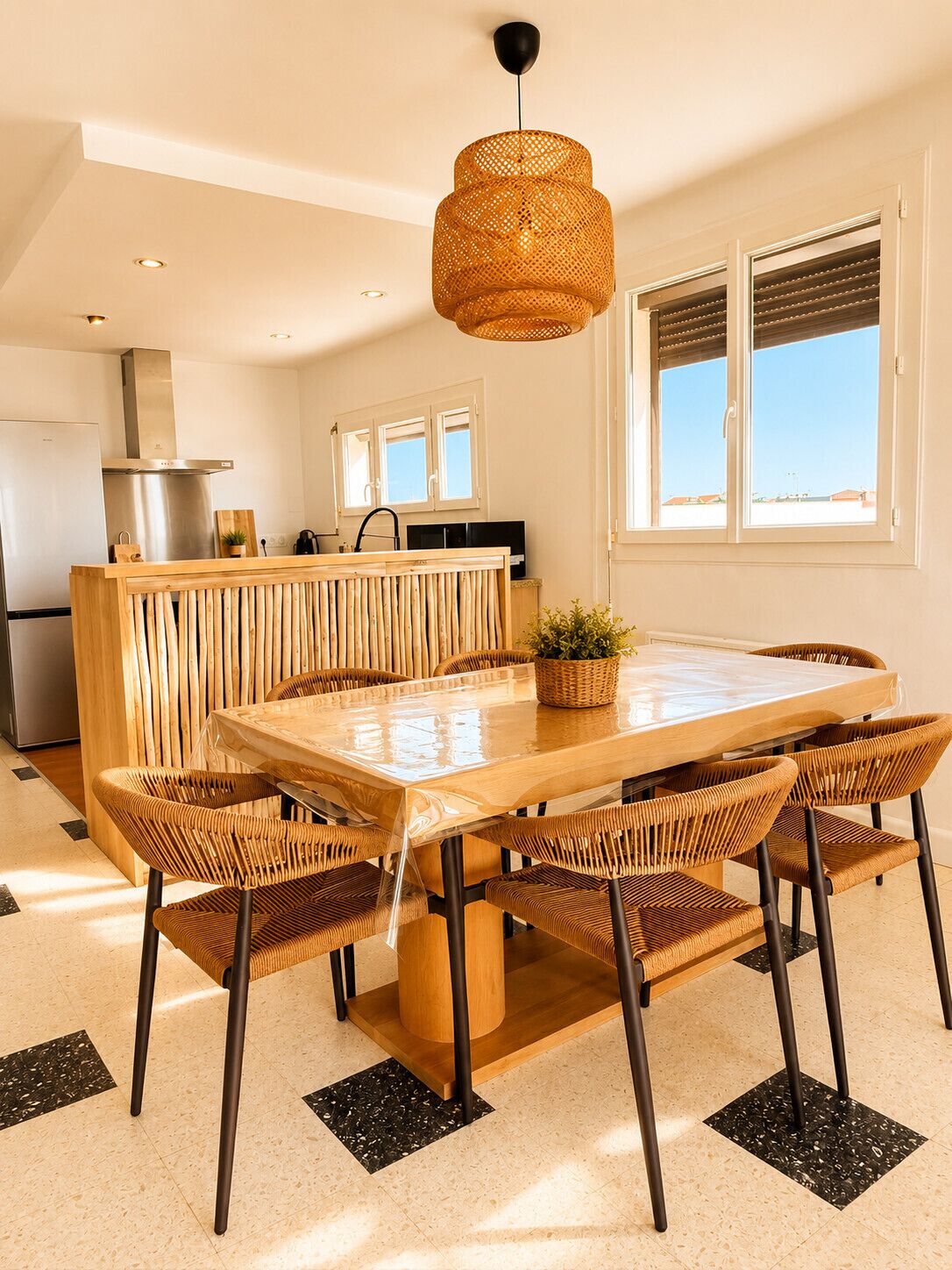 Een moderne keuken met een centraal eiland, een eethoek met een grote tafel en stoelen, en een hangende lamp.