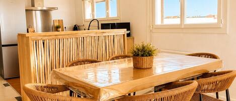 Een moderne keuken met een centraal eiland, een eethoek met een grote tafel en stoelen, en een hangende lamp.