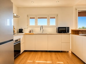 Eine moderne Küche mit weißen Schränken, einer Edelstahl-Dunstabzugshaube, einer Mikrowelle und einem Fenster über der Spüle.