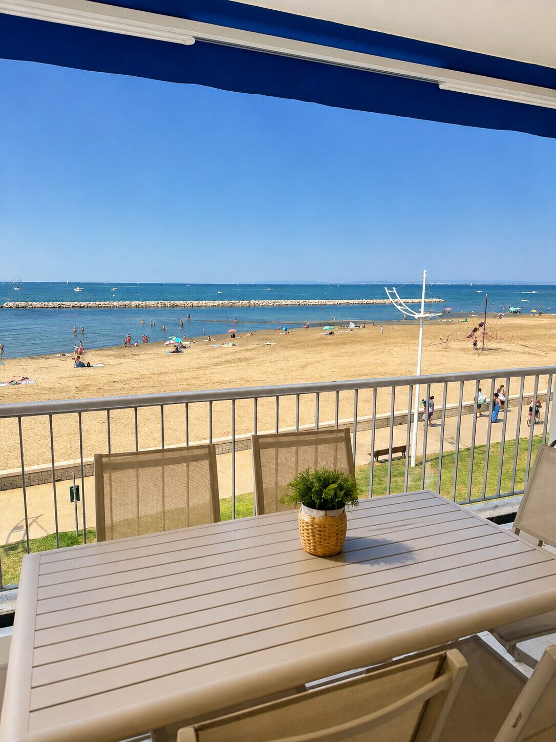 A balcony with a view of a beach, a table with chairs, and a potted plant.