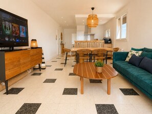 Ein modernes Wohnzimmer mit Fernseher, einer Couch, einem Esstisch und einer Küchenzeile im Hintergrund.