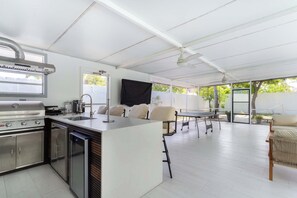 A modern kitchen with a built-in grill, a sink, and a dishwasher. There is a dining area with a table and chairs. - Near Little Havana - Pool,  WFH Space (Miami)