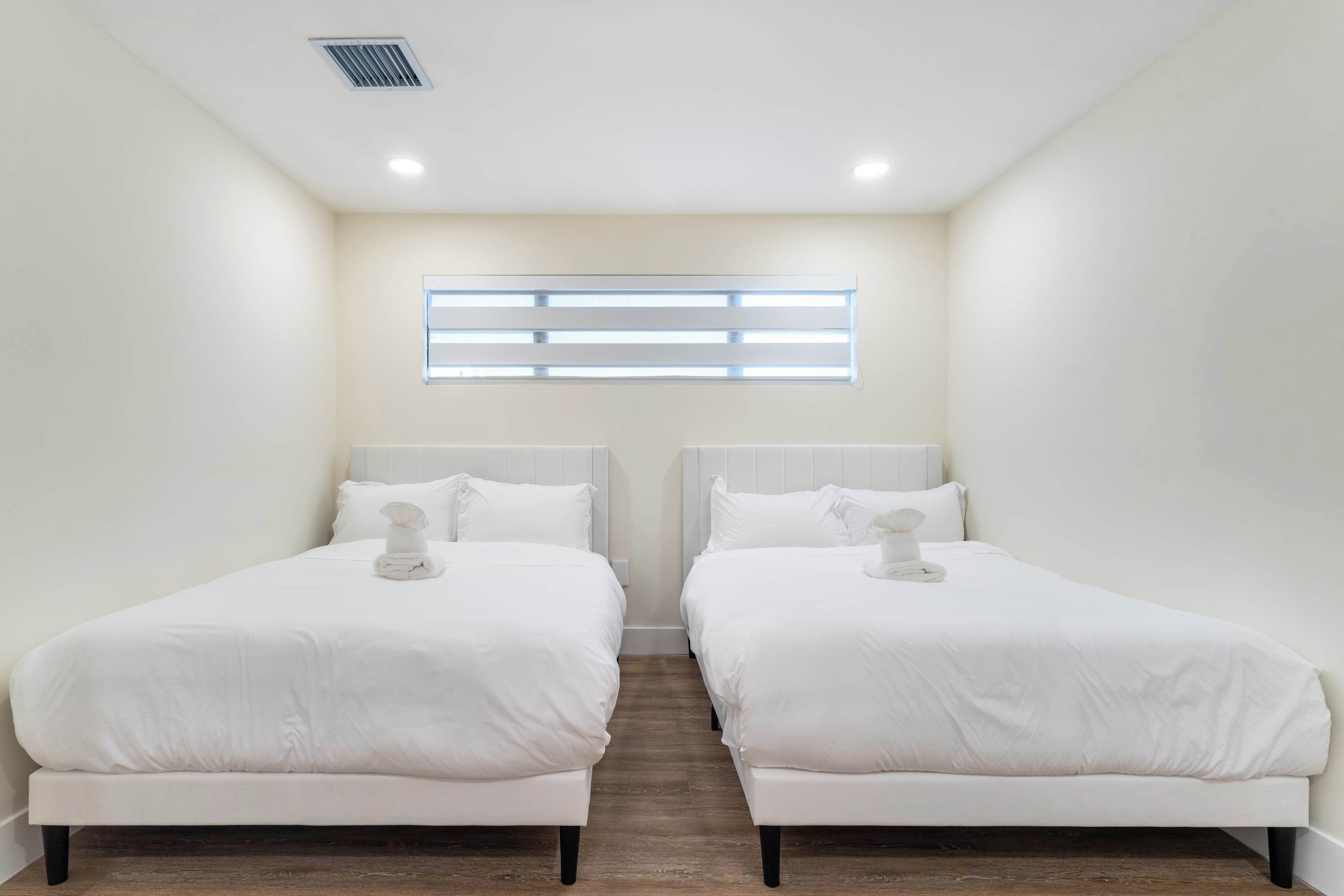 Una habitación de hotel con dos camas individuales, una ventana con persianas, un respiradero en el techo y un interruptor de luz en la pared.