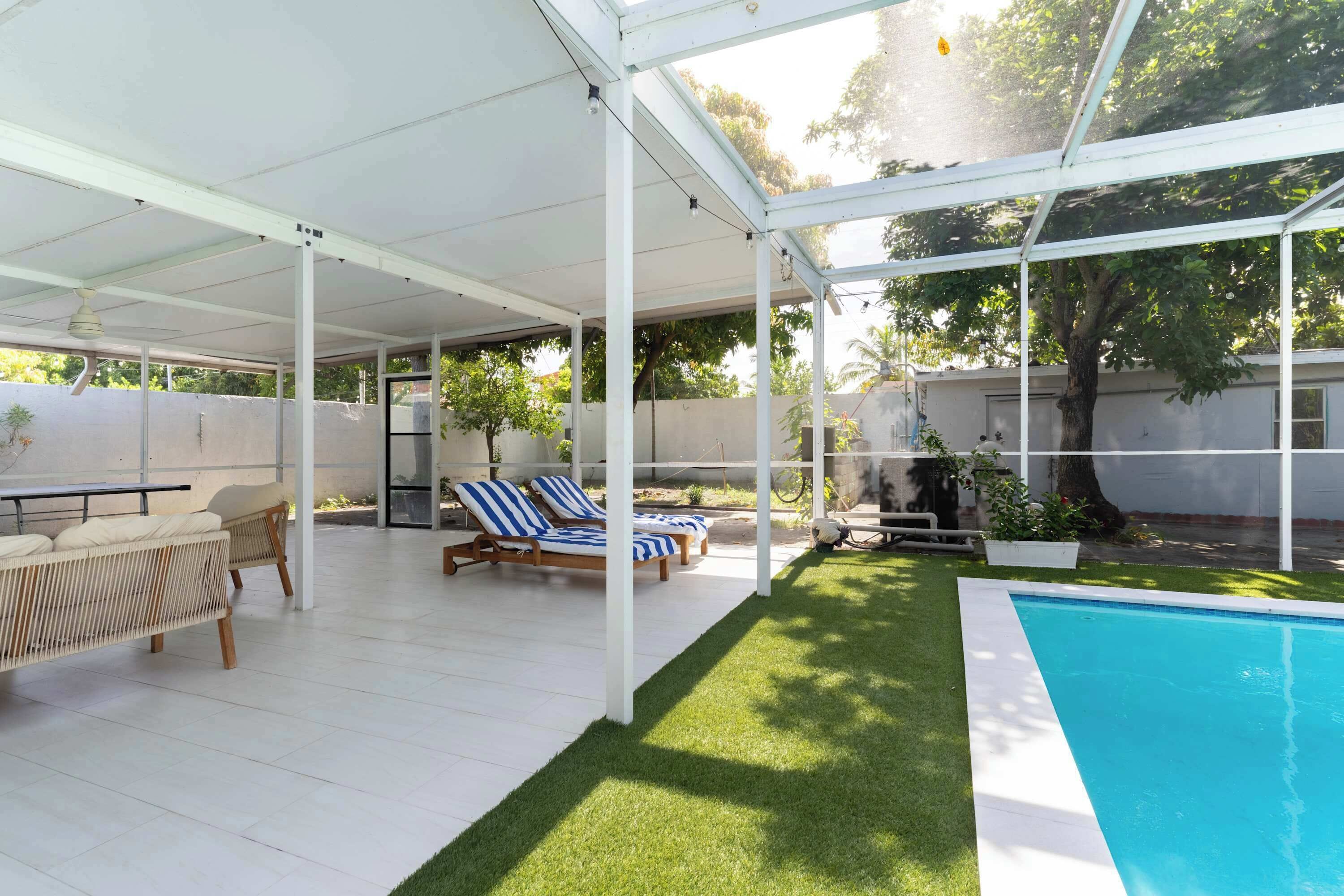 Ein überdachter Außenbereich mit Pool, Liegestühlen und einem Tisch.