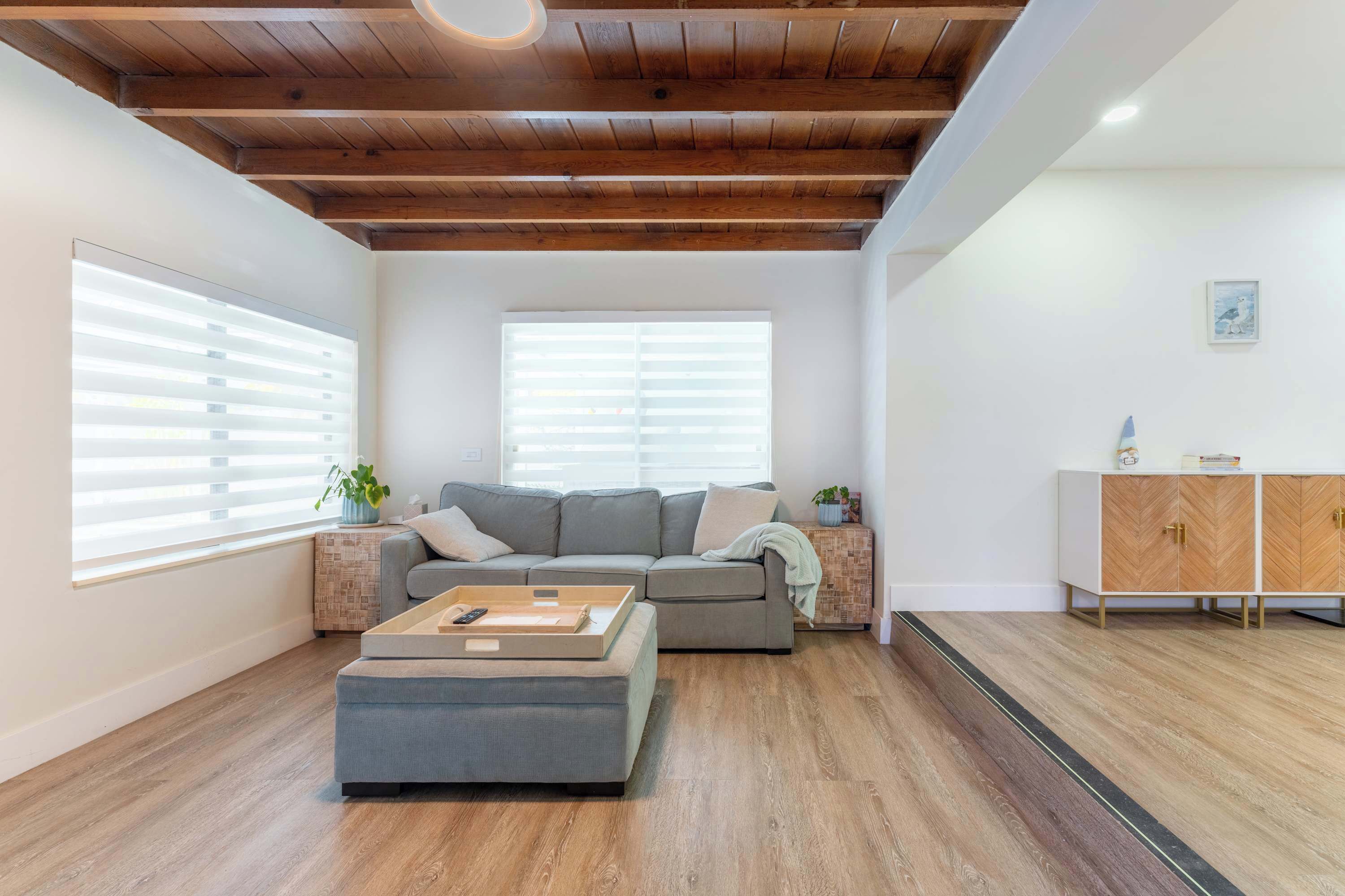 A modern living room with a wooden ceiling, a grey sofa, a coffee table, and a cabinet with herringbone-patterned doors.
