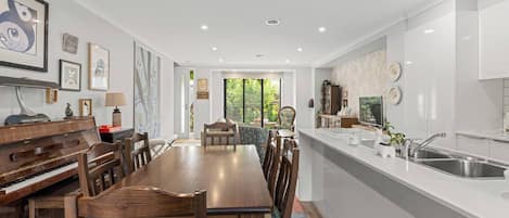 Una cocina moderna con zona de comedor, que incluye un piano, un ventanal grande y un lavamanos.