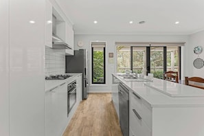 A modern kitchen with white cabinetry, a central island, and a view of greenery outside. - The Pattern House Ballarat Lakeside Creative Haven (Canadian)