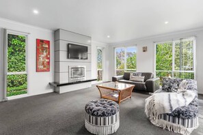 A modern living room with a fireplace, a sofa, ottomans, and a coffee table. - Greenview Bungalow Sunlit Stay near Sovereign Hill (Brown Hill)