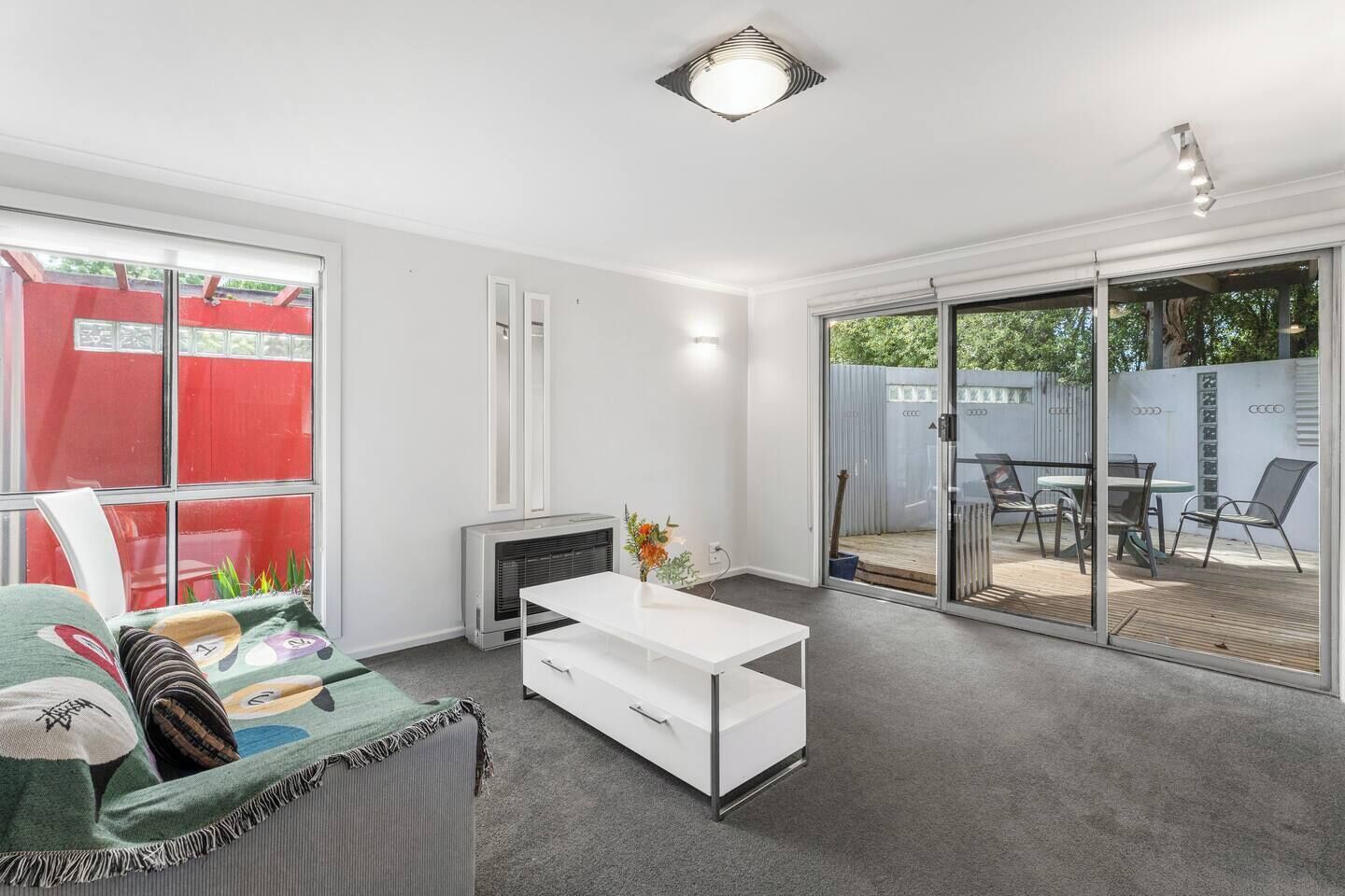Un salon moderne avec un canapé blanc, une table basse blanche et une porte-fenêtre coulissante donnant sur une terrasse extérieure avec une table et des chaises.