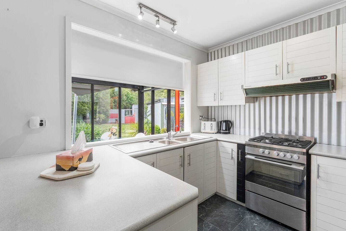 A modern kitchen with white cabinetry, a gas stove, an oven, and a large window offering a view of the outdoors.