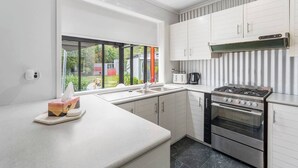 Uma cozinha moderna com armários brancos, fogão a gás, forno e uma janela grande com vista para o exterior.