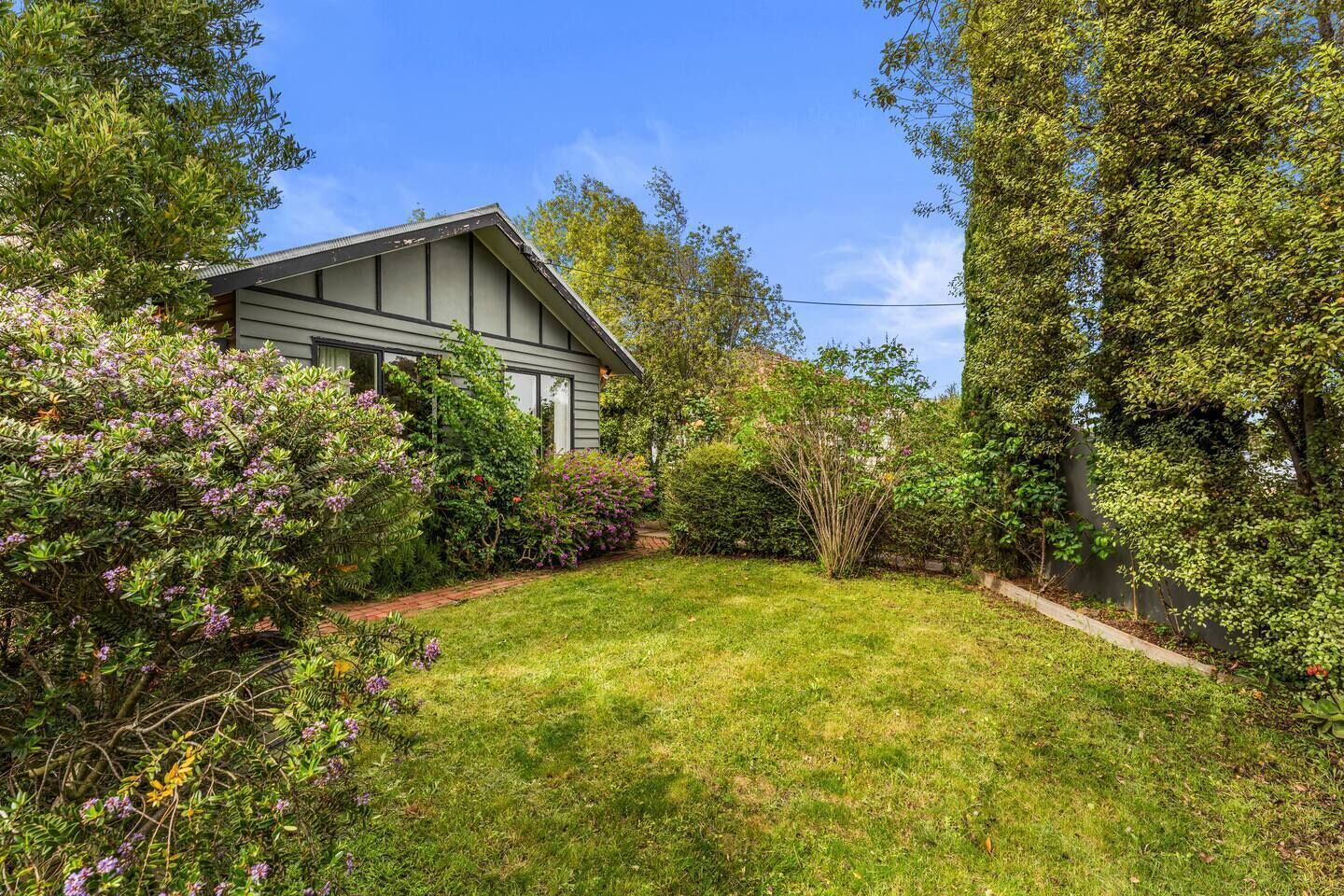 A residential property with a well-maintained lawn, a variety of flowering shrubs, and a house with a gabled roof.