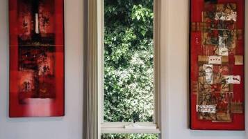 A room with a window, two artworks on the walls, and a view of greenery outside.