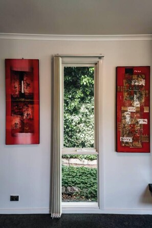 A room with a window, two artworks on the walls, and a view of greenery outside. - Greenview Bungalow Sunlit Stay near Sovereign Hill (Brown Hill)