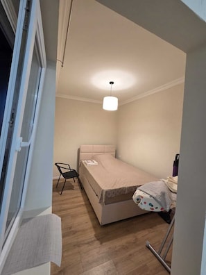 A small, single-bed room with a wooden floor, a bedside table, a chair, and a hanging light fixture. - Apartment with a sea view in Batumi, 200 m from the beach (Batumi)