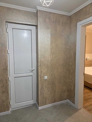 A room with a closed door, a light switch, and a partially visible bed in the adjacent room. - Apartment with a sea view in Batumi, 200 m from the beach (Batumi)
