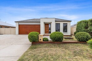 A residential house with a garage, a front door, and a small garden with trimmed bushes.