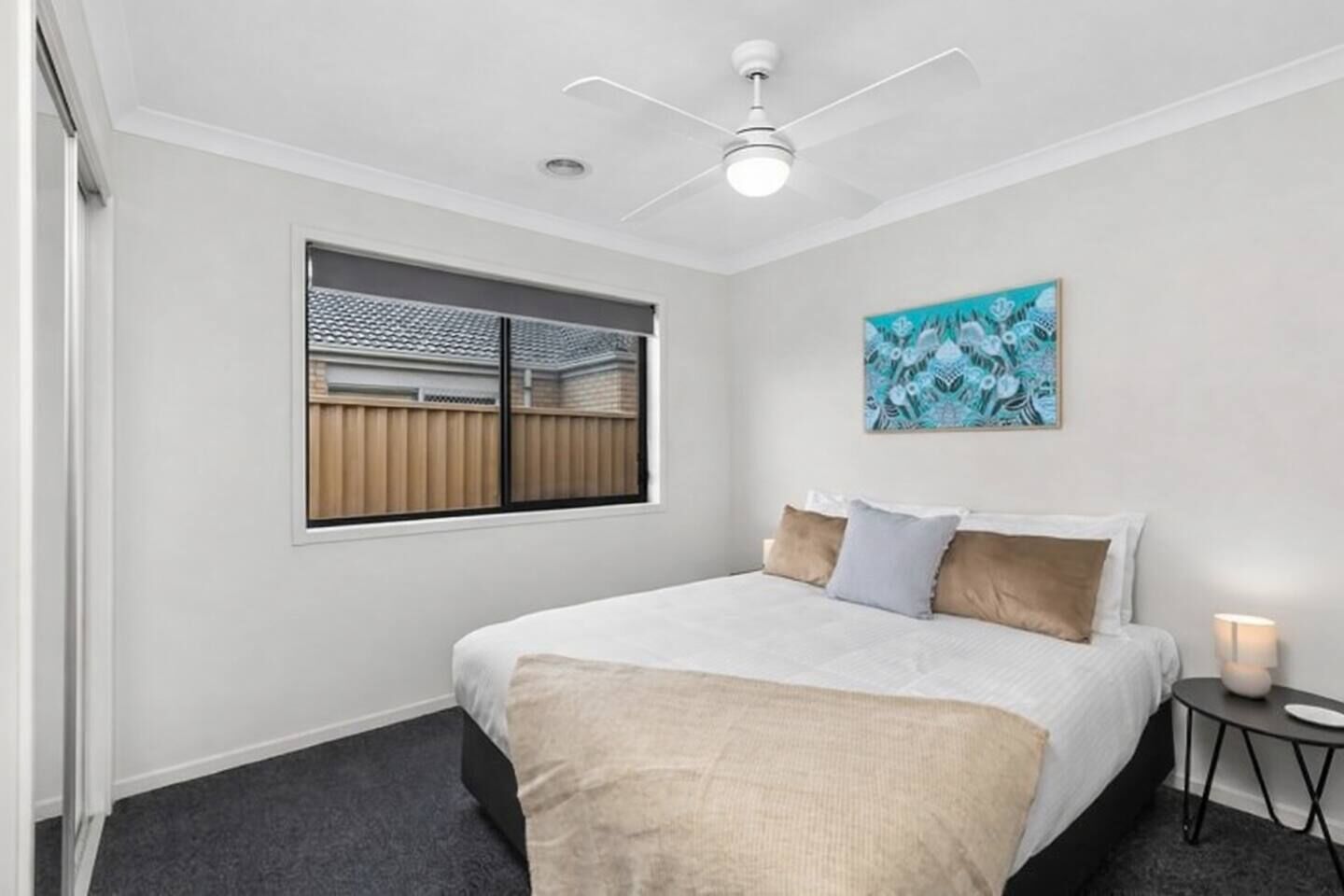 A bedroom with a bed, a window with a view, a ceiling fan, and a wall-mounted artwork.