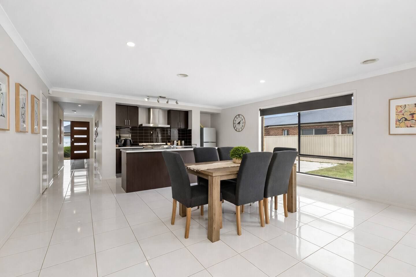 A modern kitchen with dark cabinetry, a central island, and a dining area with a wooden table and chairs.